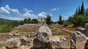 Ancient temple columns in an open field with surrounding trees and mountains in the background