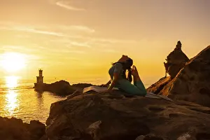 Anjaneyasana, A woman doing meditation and yoga exercises at sunset next to a lighthouse in the sea