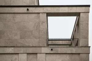 Architectural detail of a contemporary building featuring travertine cladding and a minimalist metal railing