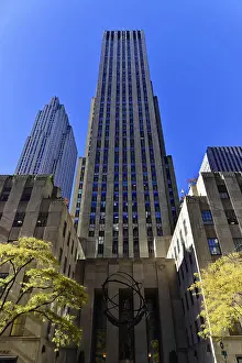 Architectural shot of a tall skyscraper against a blue sky with autumnal trees in the foreground