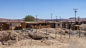 An arid landscape with simple buildings and electricity pylons under a clear sky
