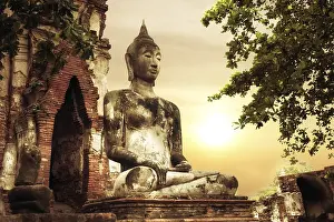 Asian religious architecture. Ancient sandstone sculpture of Buddha at Wat Mahathat ruins under sunset sky