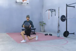 Athlete is performing lunges while holding a medicine ball in an outdoor gym