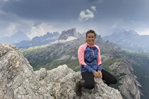 An attractive brunette mountain climber sitting on a mountain peak and smiling