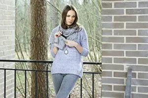 Attractive lady in sweater and scarf standing on balcony of the house in forest