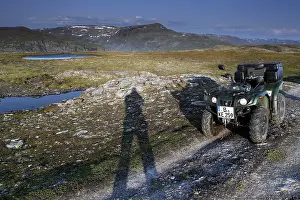 ATV is standing on a dirt road next to a long shadow of people in the vast countryside