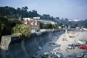 Autos und Menschen am Sandstrand vor einer grossen, gebogenen Kuestenschutzmauer, St Brelade, Jersey, Kanalinseln, 1964, Europe