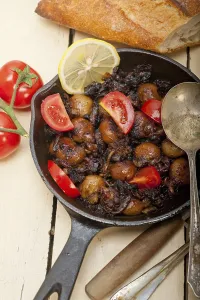 Baby cuttle fish roasted on iron skillet with tomatoes and onions over rustic wood table
