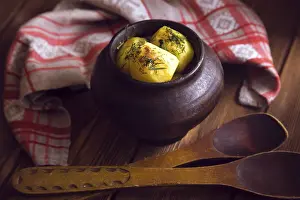 Baked potato in old pot on wooden background with pickled cabbage and cucumber