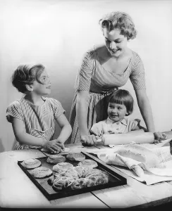 Baking in the 1950s. A mother with her children baking buns and bread together at a table