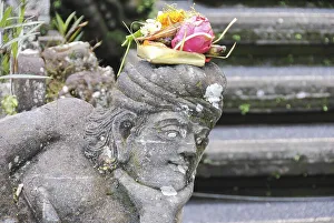 Balinese religious offering (canang sari) over a stone statue