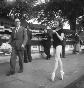 Ballerina in Paris 1952. Ellen Rasch, 1920-2015 pictured in Paris in her dancing outfit standing on her toes reading a book off a street merchants stand. Paris 1952 Kristoffersson ref BD27-7