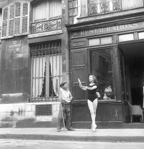Ballet dancer in the 1950s. Ellen Rasch, 1920-2015, swedish balletdancer and actress pictures in Paris France standing on her toes holding an antique outside a store while a street cleaner looks on, paused in his work