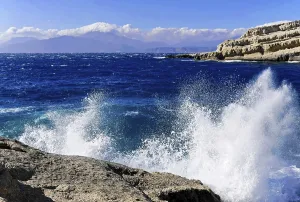 Bay, Matala beach, spray of waves crashing on rocks under a bright blue sky
