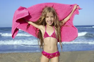 Beach little girl playing pink towel and wind in blue sea