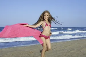 Beach little girl playing pink towel and wind in blue sea
