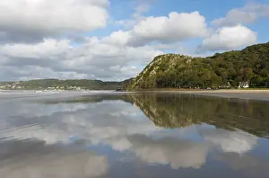 Beach with mountain backdrop and clouds reflected in the calm water