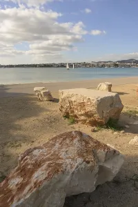 Beach scene with large rocks and a sailboat visible across the calm water