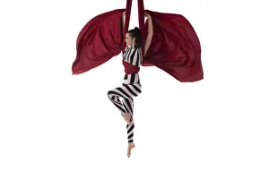 Beautiful charming slim gymnast with upped hands hanging on red material on white background
