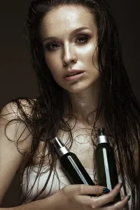 Beautiful girl with a bright make-up and wet hair and skin with bottle of cosmetic products in the hands