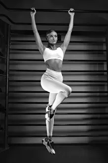 Beautiful tall blonde pulls up on the bar in the gym against the backdrop of the wall bars