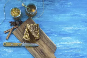 Bee pollens jar spices honeycomb piece with knife against blue textured background