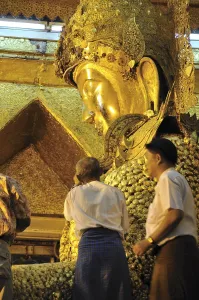 Believers sticking gold foil on a Buddha statue