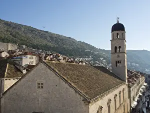 A bell tower rises above a church in a medieval town that stretches along a sunlit hill