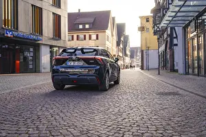 Black car on a paved street in the city with modern and historic architecture in the background at dusk