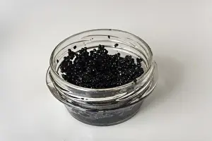 Black caviar in a glass jar on white glass