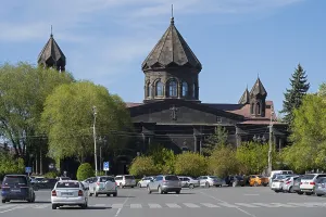 A black church with old architecture and parked cars in a green setting