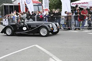 A black convertible classic car at a racing event with spectators in the background