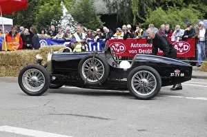 A black historic racing car is pushed by a man at a classic car event