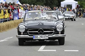 A black Mercedes-Benz convertible classic car drives on a rally surrounded by the public