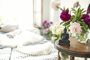 Black stone Buddha Figure On cozy light room background on the little table with peony flowers