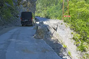 Framed Print : A black van drives on a remote road along a steep cliff with green vegetation