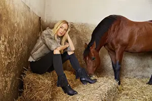 Blond woman on an indoor stable with a brown horse on straw bale