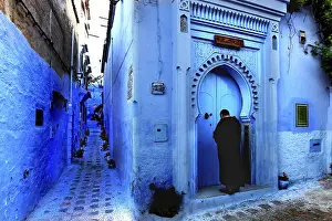 Blue alley with traditional Moroccan gate and a person in the medina of Chefchaouen
