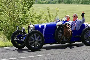 Blue classic car with two men on a country road under a sunny sky
