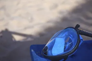 Blue diving mask resting on a surface with sandy beach in the background