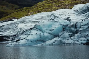 Blue glacier body resting beside a water body with rolling hills