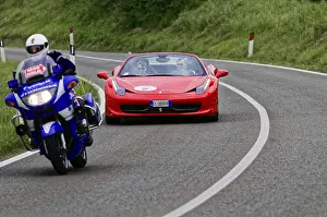 Blue motorbike overtakes red Ferrari convertible on winding road