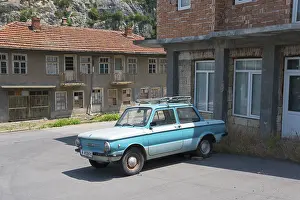 A blue retro car parked in front of dilapidated buildings under a clear sky