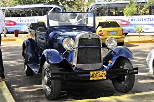 A blue vintage car parked under the sun with its licence plate visible