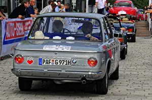 BMW, rear view of a grey classic car at a car event surrounded by people and banners