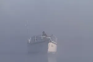 A boat sails through misty water with wind turbines in the background