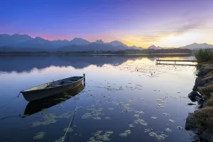Boats at a jetty on a calm lake at sunset with mountains in the background