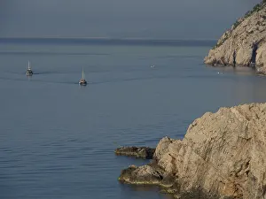 Two boats sail on the calm sea along a rocky coast