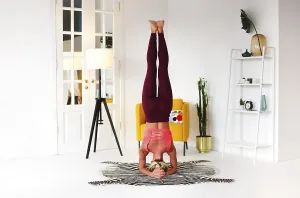 Full body of focused slim female female performing handstand near wall while practicing yoga in light room