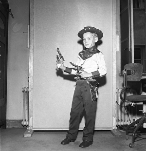 Boy in the 1950s. A boy is dressed in cowboy clothes, shirt, gun holster and cowboy hat and holds two toy revolvers. 1950. Kristoffersson ref AZ47-10